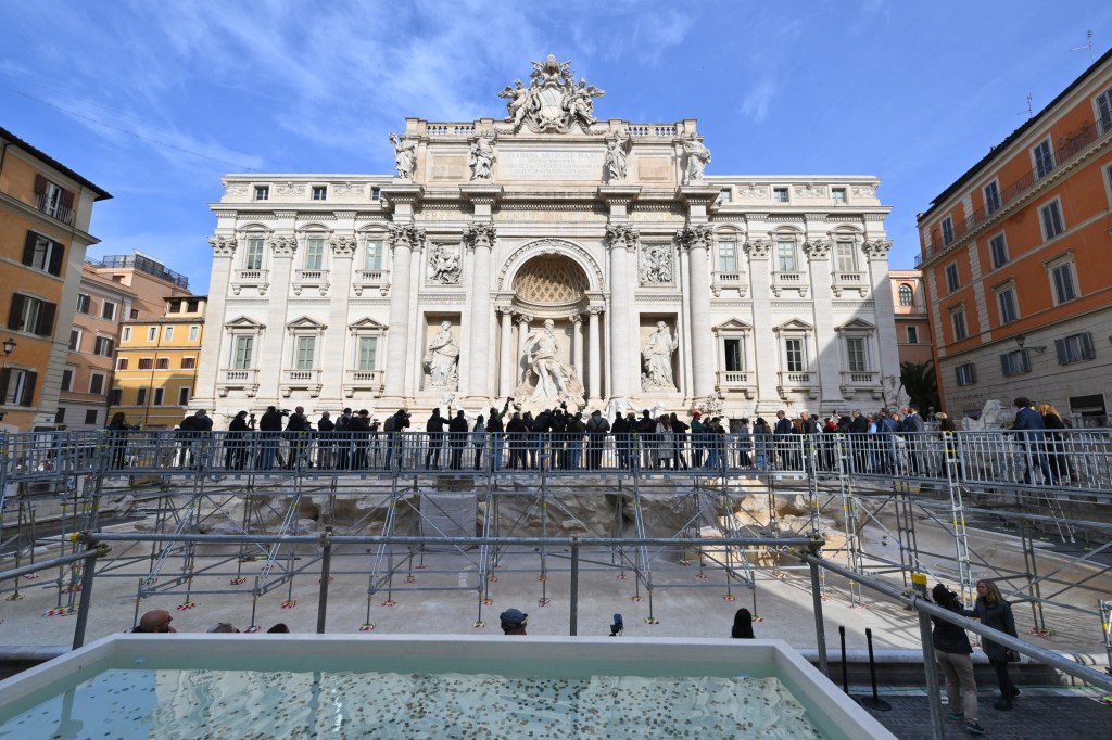 Tourists throwing coins through the scaffolding into a makeshift pool at the Trevi Fountain, Rome during renovation works in 2024